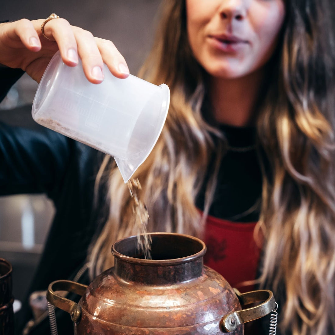 Person pouring botanicals into still to make gin. Photography by CJ Maddock